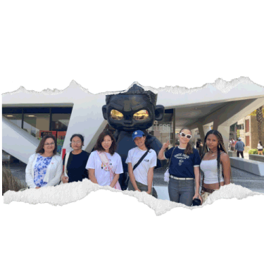 Ripped effect image of 5 interns and a mother posing in front of a statue of a comic figure in black with gold eyes